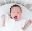 Yawning newborn baby lying in a white crib.