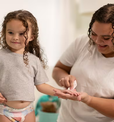 Una madre alegre limpia suavemente la mano de su hija sonriente con una toallita húmeda suave, creando un momento conmovedor lleno de amor y cuidado.