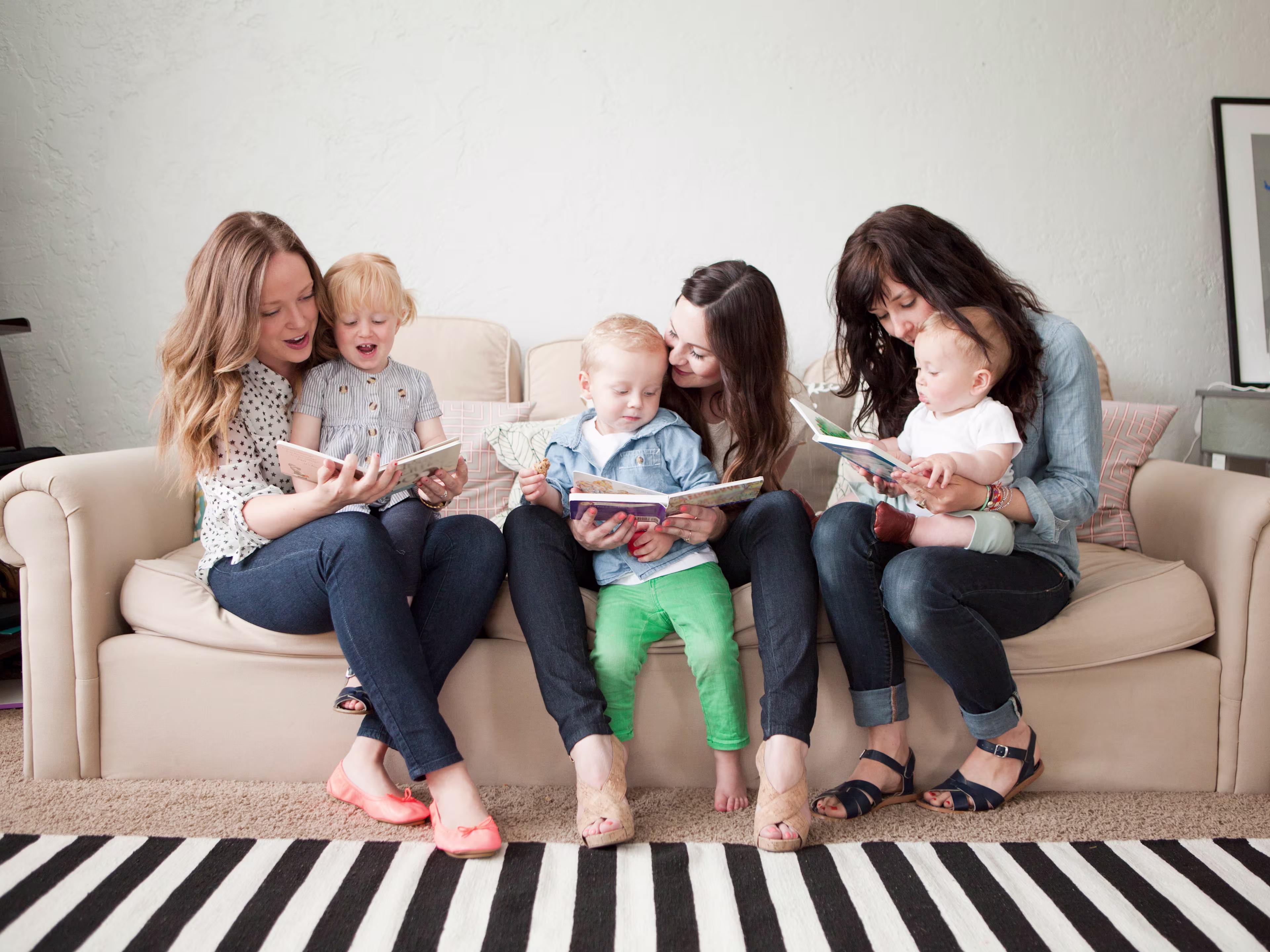 Image of three adults sitting on a couch reading books to their kid sitting in their laps.