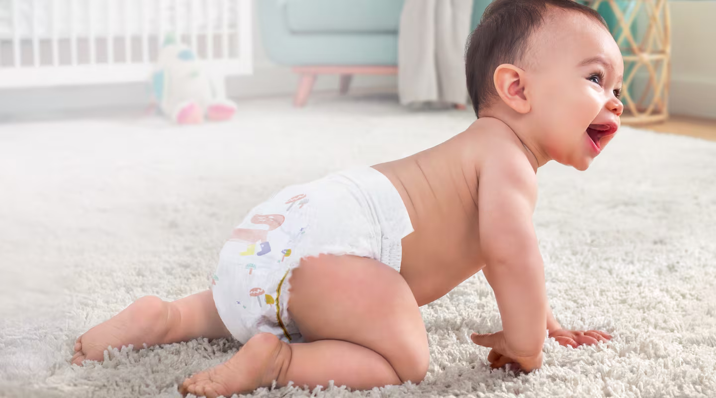 Czołgający się, roześmiany niemowlak w pieluszce Pampers