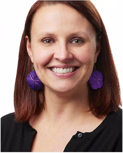A female scientist with brown hair and purple earrings smiles.
