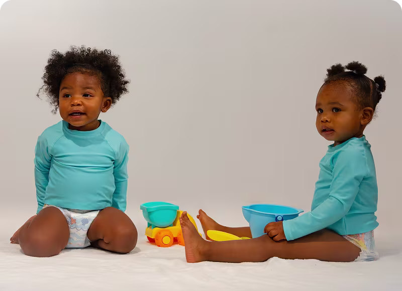 Dos niños pequeños con Pampers Splashers se sientan juntos con algunos juguetes coloridos.