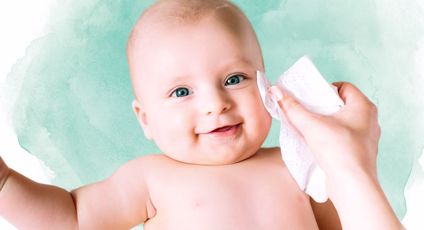 En närbild av ett spädbarns ansikte medan en hand försiktigt torkar deras kind med en Pampers Harmonie Aqua-våtservett.
