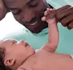 Father gently holding baby's hand, both smiling.