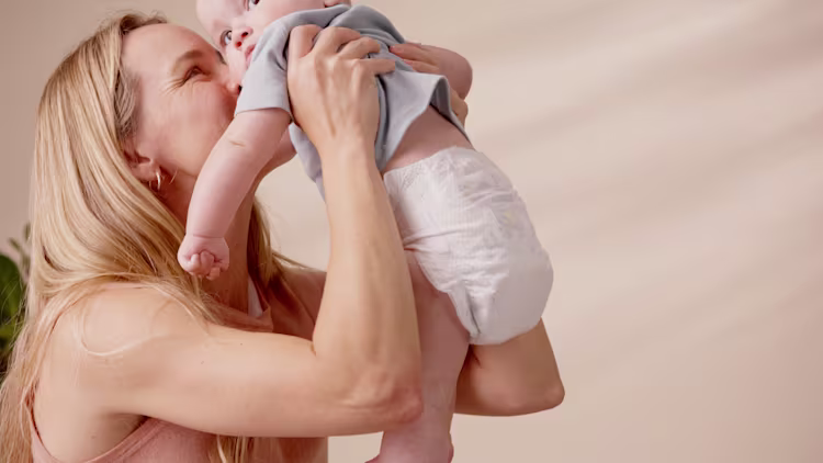 Une mère soulève son bébé en couche et l’embrasse tendrement, tous deux souriant.