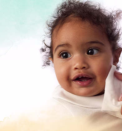 Um close-up do rosto de um bebé enquanto uma mão lhe limpa suavemente a bochecha com uma toalhita Dodot Pure Cuida & Protege.