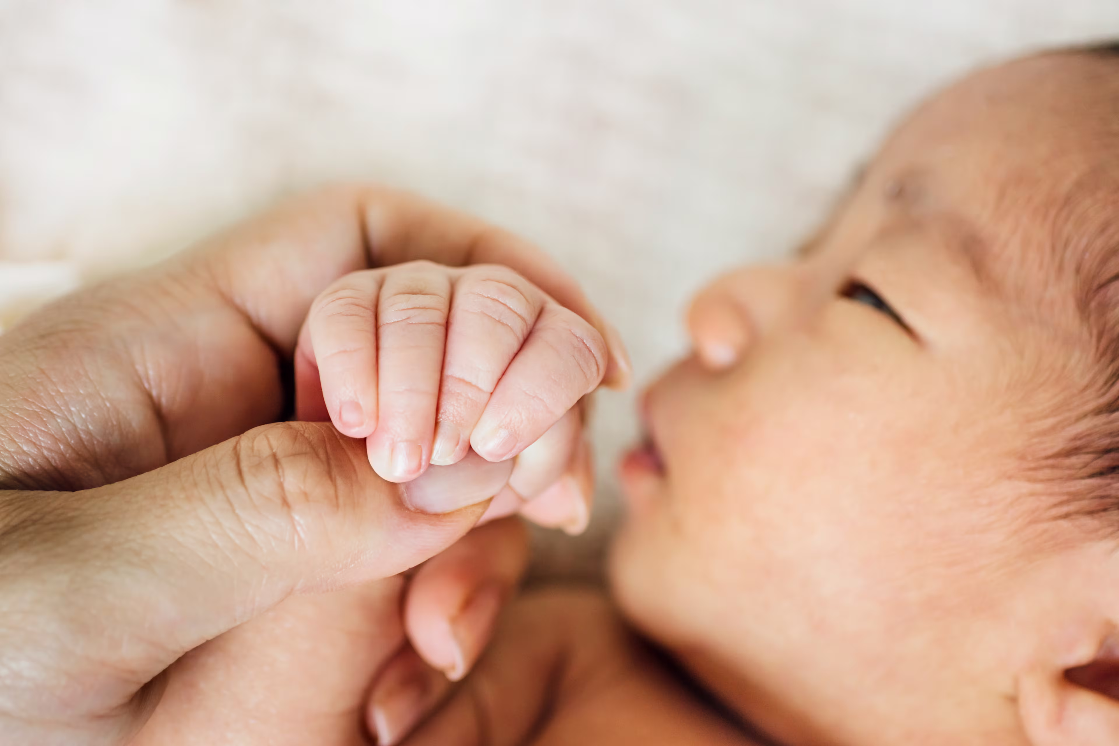 Mom holding her baby's hand while the baby looks away from the camera.
