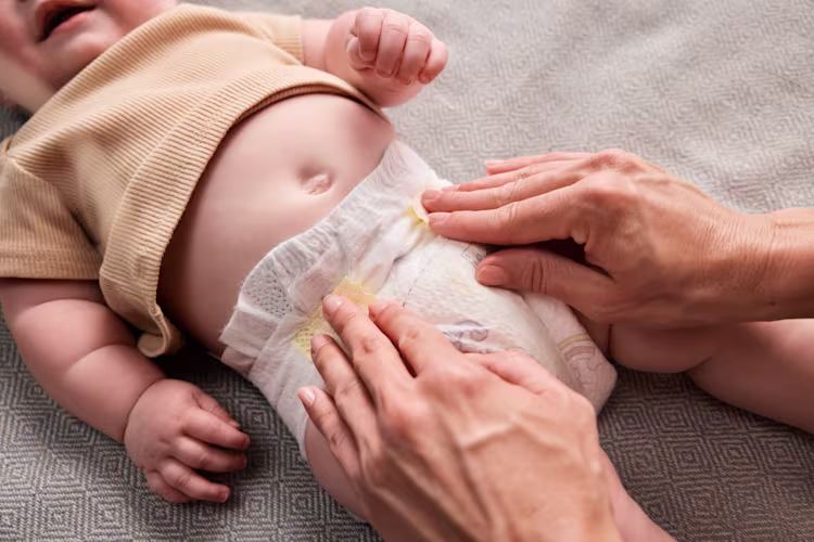 Un parent met une nouvelle couche à un bébé allongé sur un lit, tandis que le bébé sourit et bouge joyeusement.