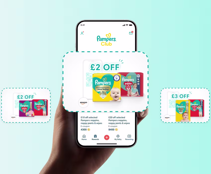 Hand holding a phone showing the Pampers Club App homescreen
