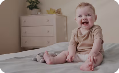 Baby smiling sitting up on a bed