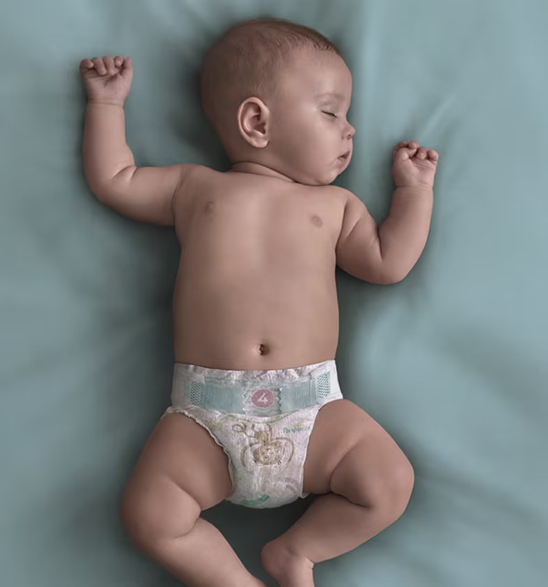 Un bébé portant une couche Pampers dort sur le dos sur une couverture turquoise.