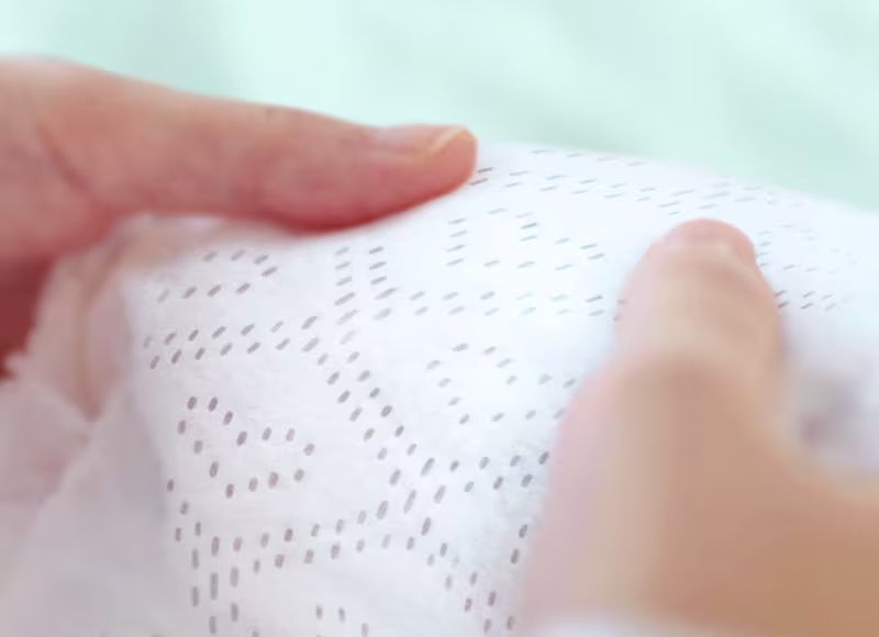 Зближений кадр показує дві руки, що ніжно тримають підгузок Pampers із м'якою текстурою, підкреслюючи його крапчастий візерунок і пухнасте відчуття. Зближений кадр показує дві руки, що ніжно тримають підгузок Pampers із м'якою текстурою, підкреслюючи його крапчастий візерунок і пухнасте відчуття.