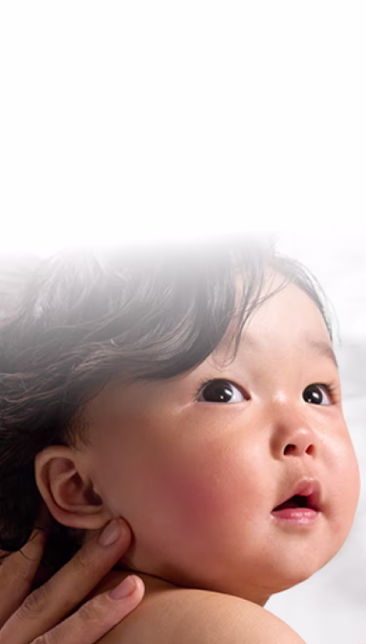Eine Mutter hält ein Baby auf dem Arm, der Hintergrund zeigt die Waben-Struktur der Pampers® Aqua Soft Touch Feuchttücher