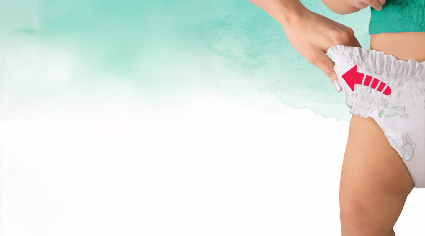 En närbild av en persons hand som drar upp toppen av en babys blöja, som är prydd med små kanin- och morotsmotiv, över barnets höft.