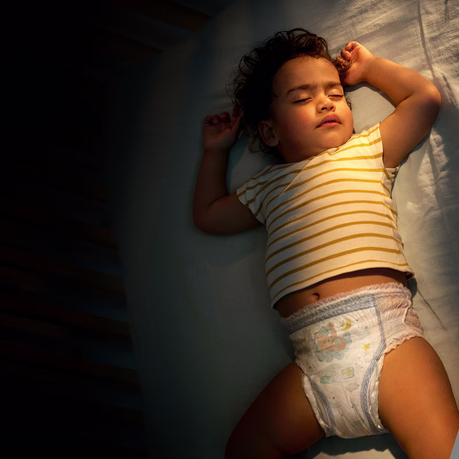 Un enfant portant un t-shirt jaune et une culotte Pampers dort paisiblement sur une couverture bleu. Un enfant portant un t-shirt jaune et une culotte Pampers dort paisiblement sur une couverture bleu.