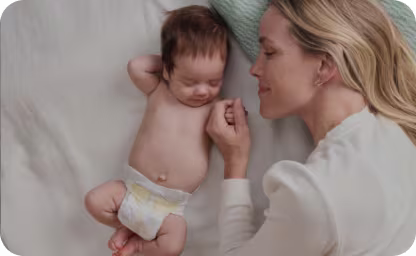 Mama leży z dzieckiem, które ma założoną pieluszkę Pampers.