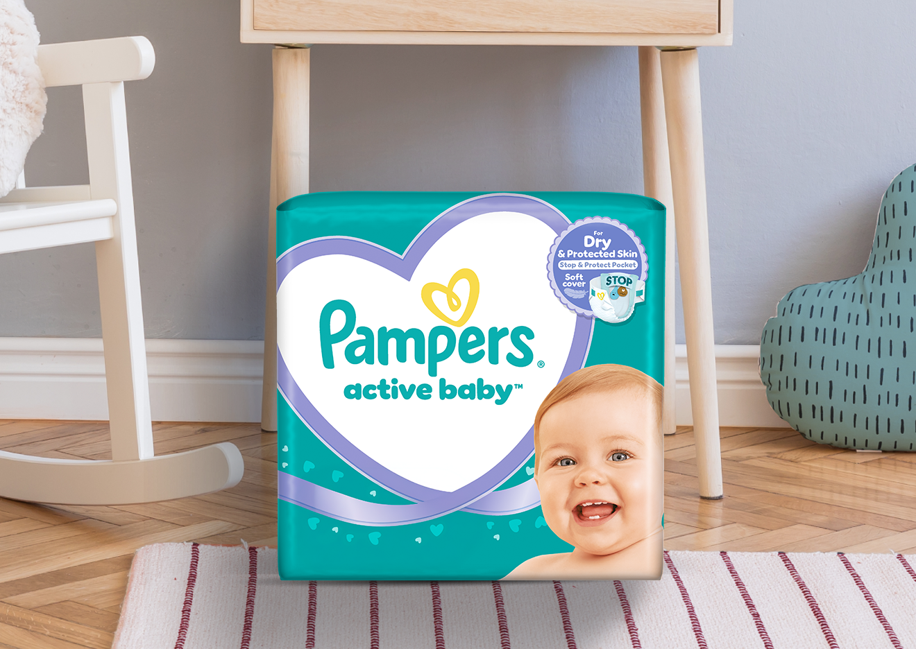 Imagine cu o cameră de copil în care se vede un pătuț, un ursuleț și pachetul de Pampers Active Baby.
