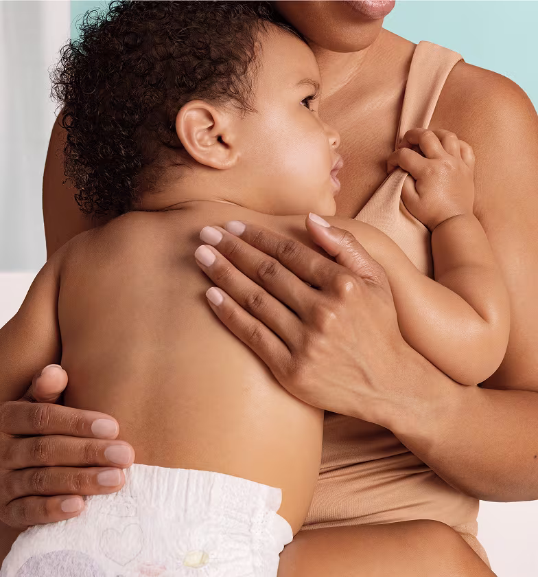 Uma imagem em primeiro plano mostra uma mãe a segurar o seu bebé junto ao peito num abraço terno. Uma imagem em primeiro plano mostra uma mãe a segurar o seu bebé junto ao peito num abraço terno.