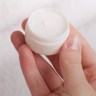 Close up of a parents hand holding a little container with cream filled in. 