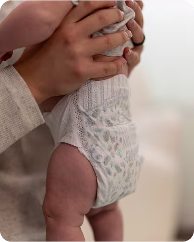 A parent gently holding up their baby wearing a Pampers Pure diaper