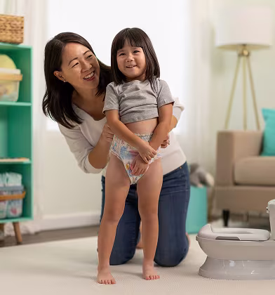 A loving mother kneels beside her cheerful toddler, who is proudly demonstrating their potty training skills. The bright, colorful room is filled with playful decor, creating a joyful atmosphere that celebrates this important milestone.