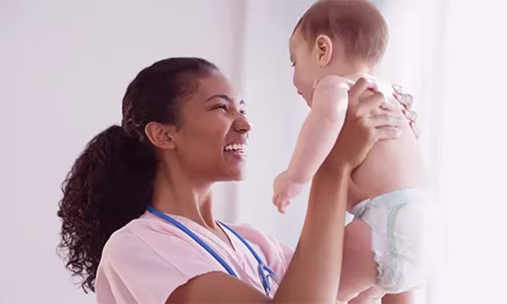 A nurse holds a baby in her arms and smiles.