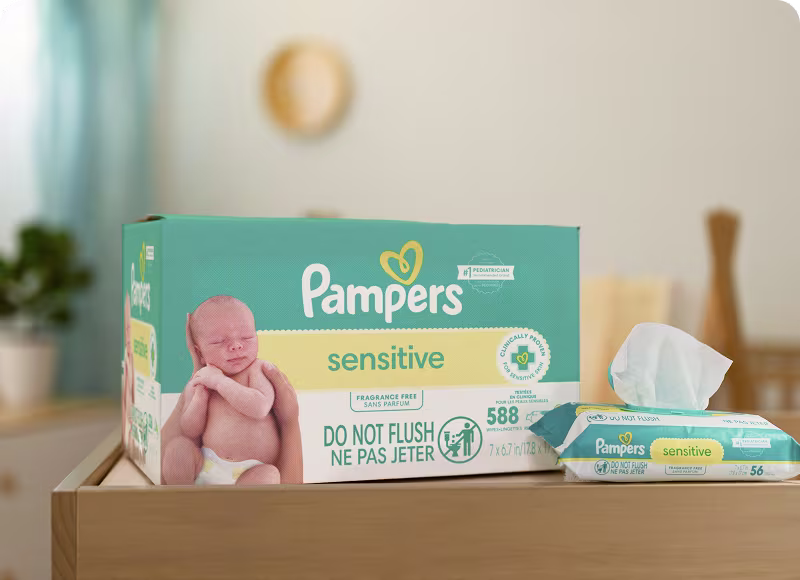 Una caja y un paquete individual de toallitas Pampers Sensitive sobre una mesa para cambiar pañales en una habitación de bebé Una caja y un paquete individual de toallitas Pampers Sensitive sobre una mesa para cambiar pañales en una habitación de bebé