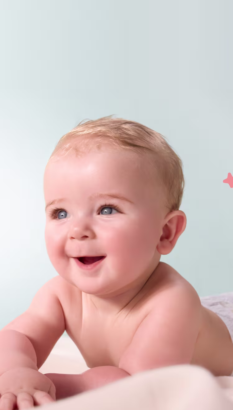 Um bebé feliz com olhos azuis, que usa uma fralda branca, está deitado de barriga para baixo e sorri enquanto olha para cima e para um lado.