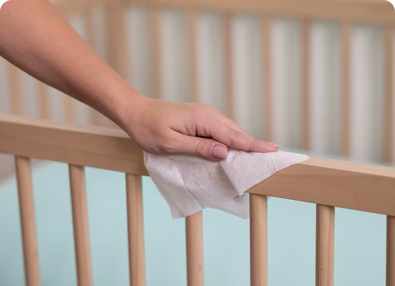 Mamá limpiando el borde de la cuna de su hijo con una toallita húmeda Mamá limpiando el borde de la cuna de su hijo con una toallita húmeda