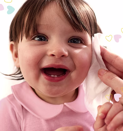 En närbild av ett spädbarns ansikte medan en hand försiktigt torkar deras kind med en Pampers Sensitive New Baby-våtservett.