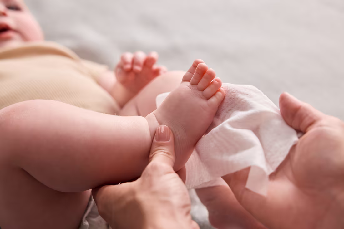 Eine Person reinigt die Füße eines liegenden Babys vorsichtig mit einem Feuchttuch.