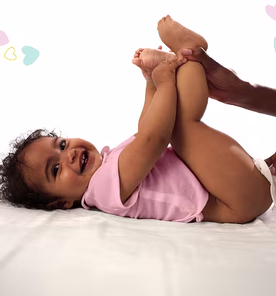 Vauva makaa selällään valkoisella pinnalla ja pitää jalkojaan ylhäällä samalla kun vanhempi käyttää kosteuspyyhettä puhdistaakseen vauvan takapuolen. Vauva makaa selällään valkoisella pinnalla ja pitää jalkojaan ylhäällä samalla kun vanhempi käyttää kosteuspyyhettä puhdistaakseen vauvan takapuolen.