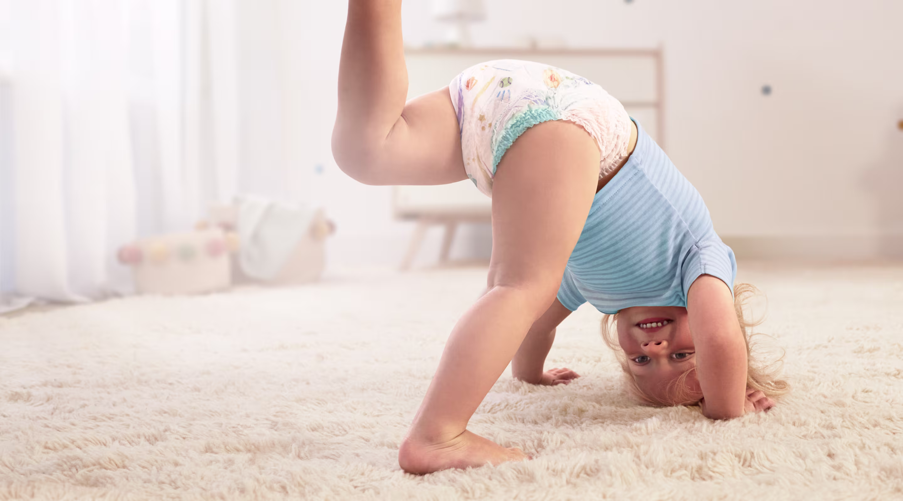 Een baby die een Pampers® Baby-Dry™ Pants draagt, doet een handstand en steekt één been in de lucht.