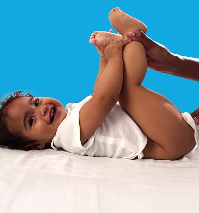 Um bebé está deitado de costas sobre uma superfície branca, levantando os pés enquanto um pai utiliza uma toalhita para limpar o rabo do bebé.