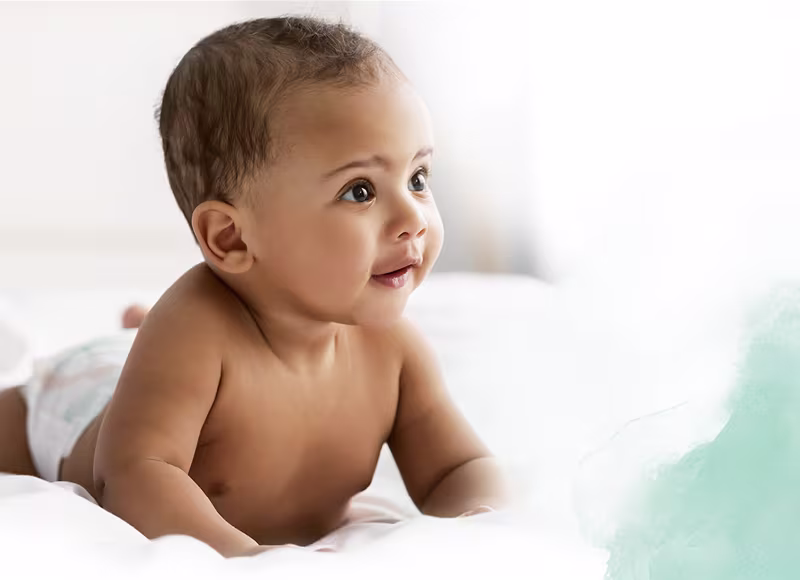 Um bebé que só usa uma fralda Dodot está deitado de barriga para baixo sobre um lençol branco.