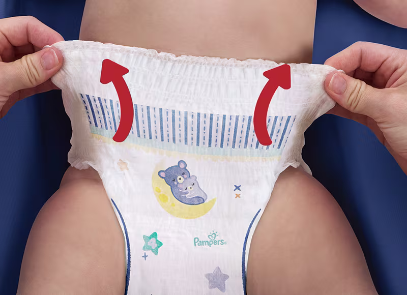 Prim-plan cu două mâini care întind ușor banda de la scutecul Pampers pe care îl poartă un bebeluș.