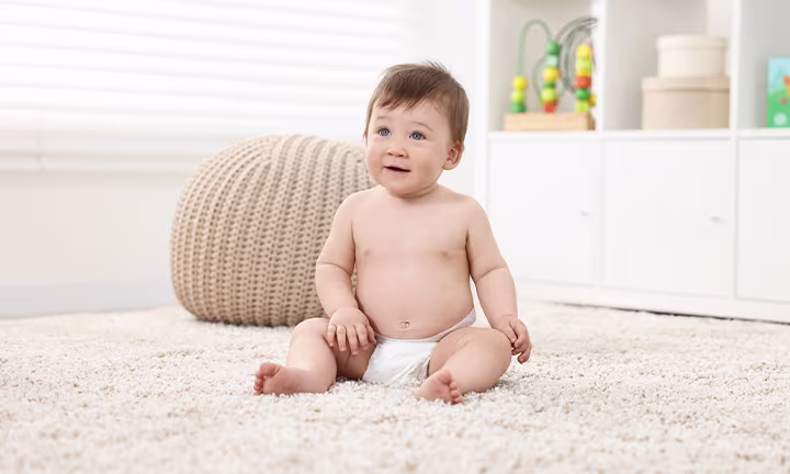 Baby sitting on a rug in diapers