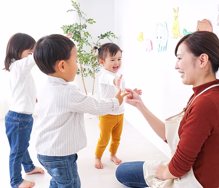 Teacher interacting with smiling toddlers in a bright classroom, encouraging play and learning.