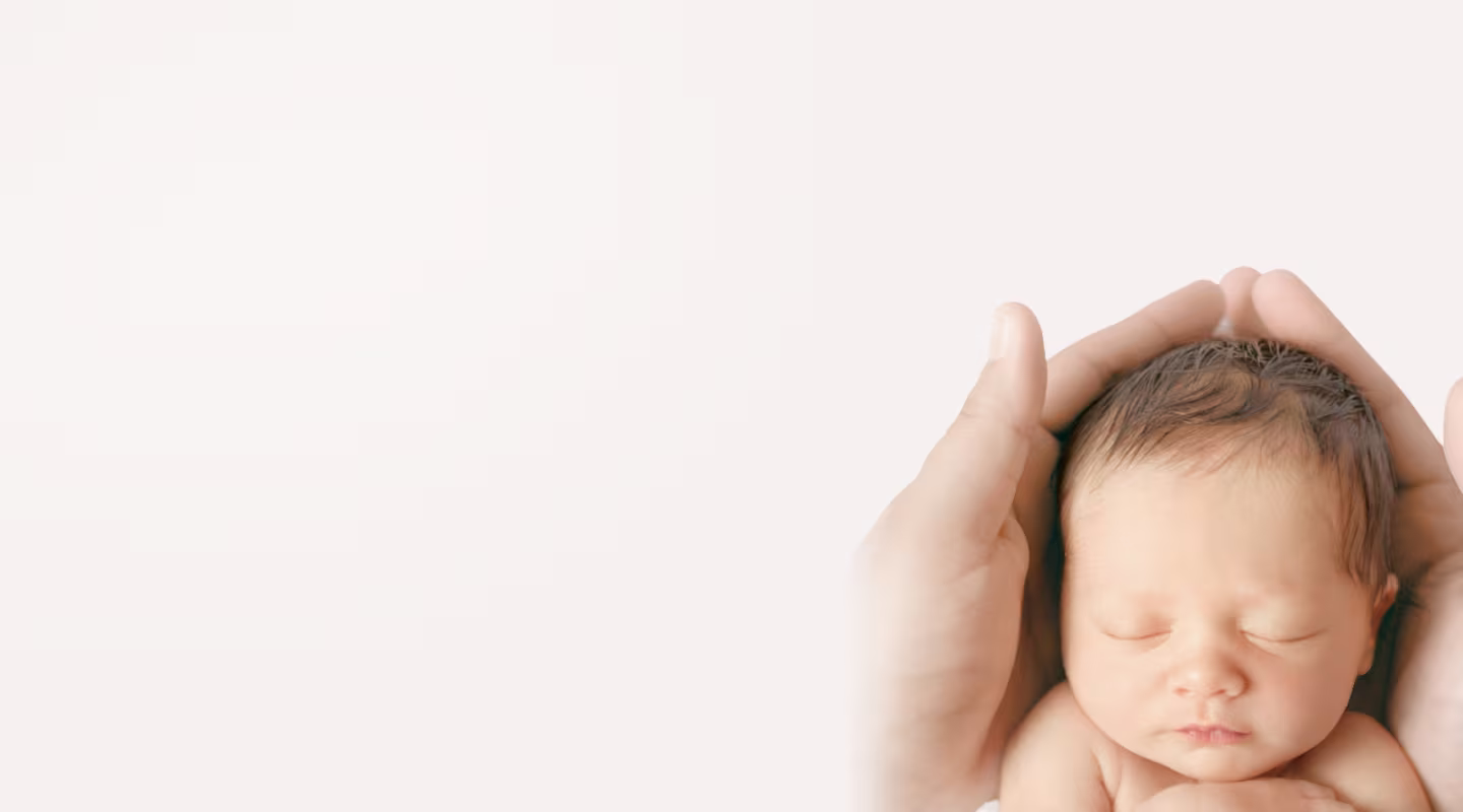 A smiling mother wearing a hospital gown holds a sleeping newborn baby close to her chest. 