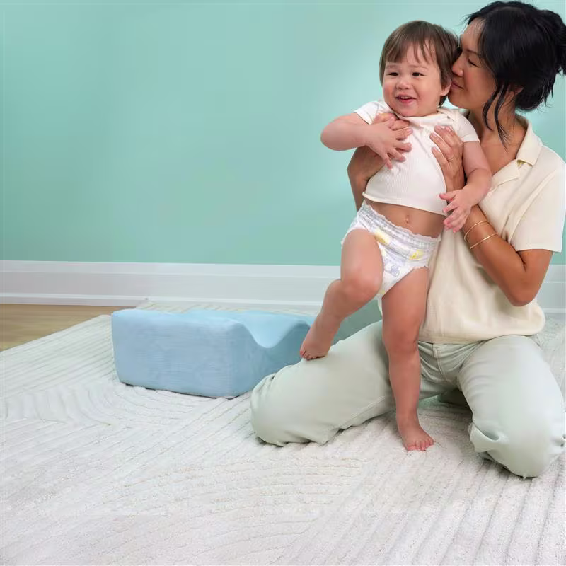 A mom wearing a yellow shirt sits in the nursery, lovingly holding her baby wearing a Swaddlers 360° pull on diaper