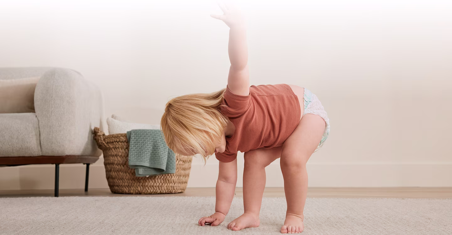 Un niño pequeño camina sobre una alfombra de color claro frente a un sofá gris.