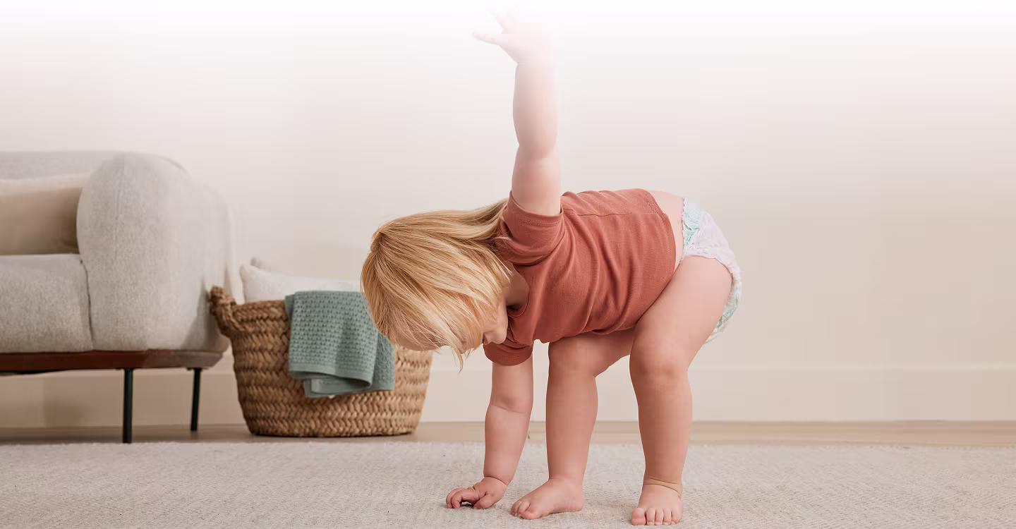 Un niño pequeño camina sobre una alfombra de color claro frente a un sofá gris.
