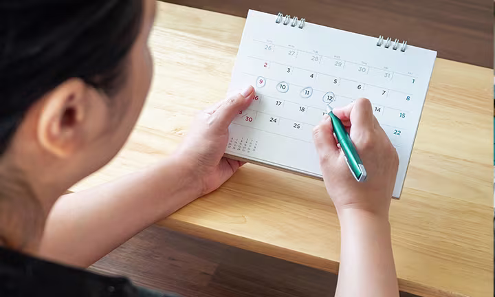 A person circling dates on a calendar/planner to track menstrual cycle