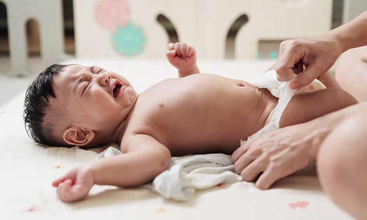 Baby crying during a diaper change, with a caregiver gently adjusting the diaper.