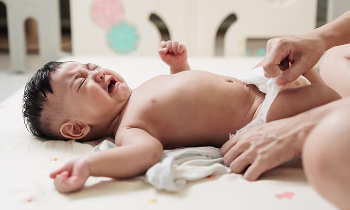 Baby crying during a diaper change, with a caregiver gently adjusting the diaper.