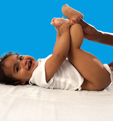 Un bebé está tumbado de espaldas sobre una superficie blanca, levantando los pies mientras un padre utiliza una toallita para limpiar el trasero del bebé.