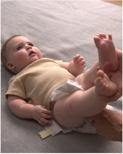 Un bebé alegre sonríe mientras su padre le quita el pañal, preparándose para un cambio de pañal.