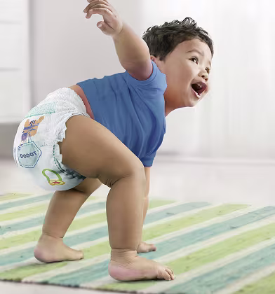 Um bebé com uma fralda-cueca e uma camisola azul, com os braços levantados, a boca aberta e os olhos a olhar para cima.