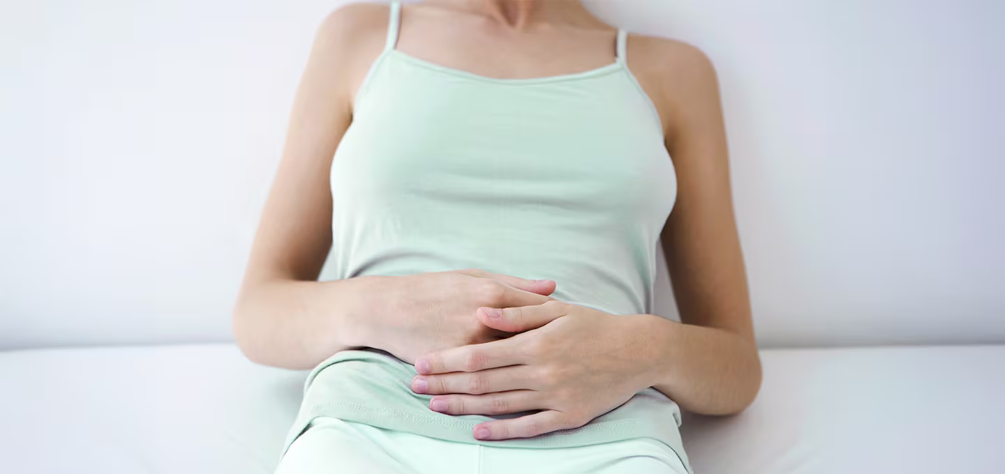 Frau liegt entspannt mit Händen auf dem Unterbauch, Symbolbild für Einnistungsblutung in der frühen Schwangerschaft.