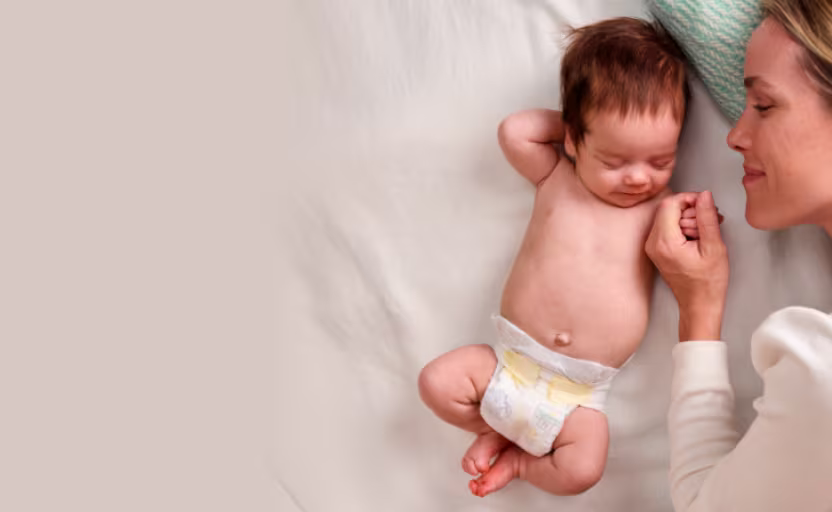Mama liegt mit dem Baby, das eine Pampers-Windel trägt